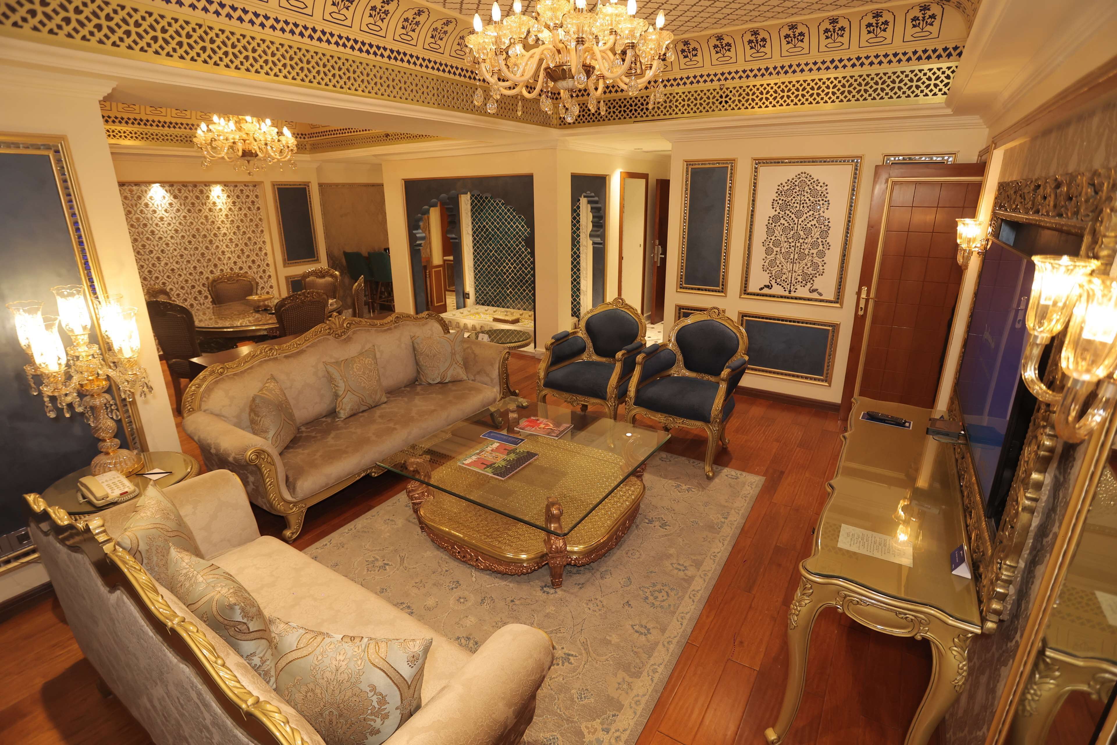 A luxurious living room with ornate furniture, a chandelier, and decorative wall panels.