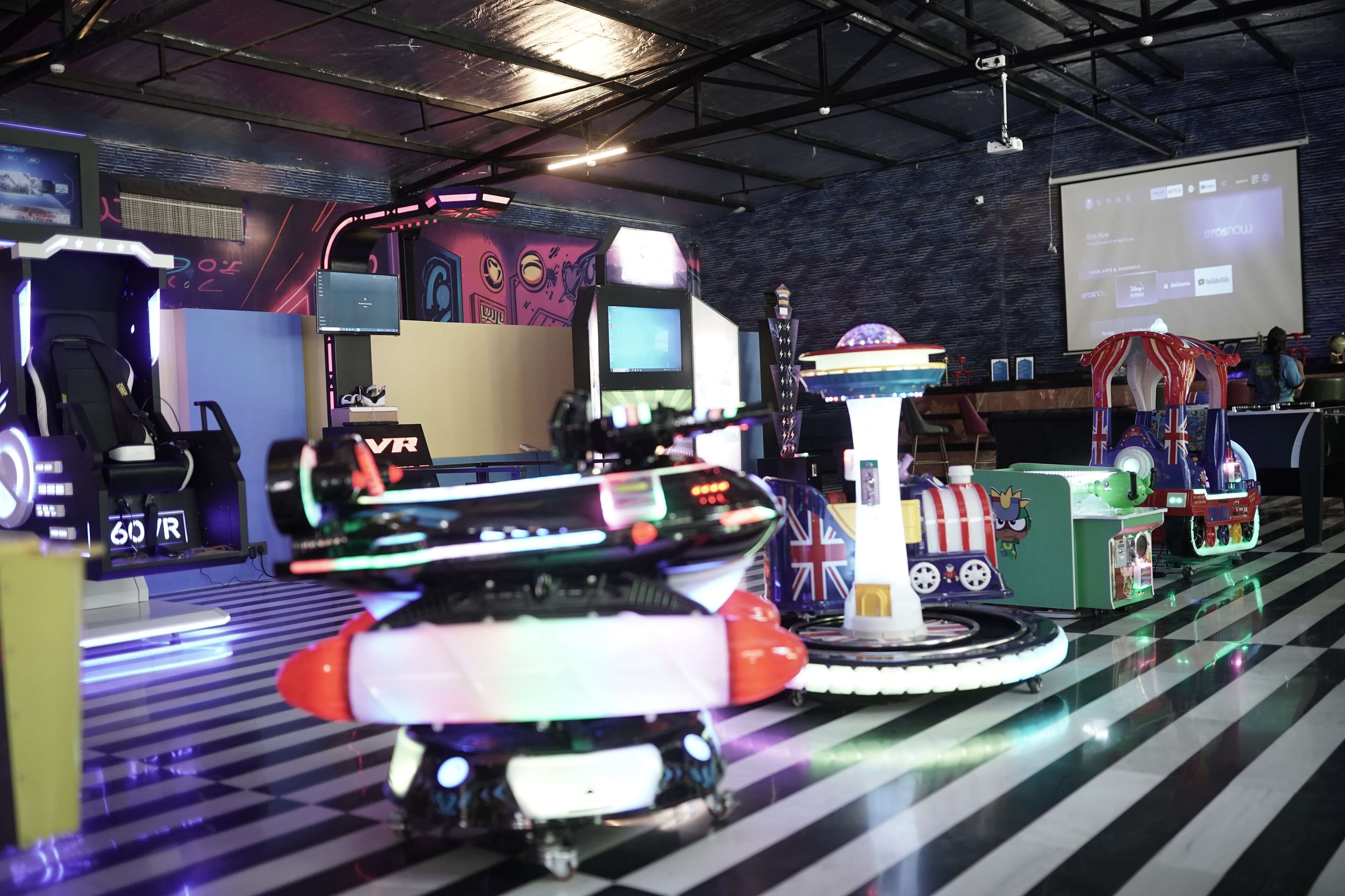 Une salle d’arcade intérieure avec différents jeux et un écran de projection en arrière-plan.