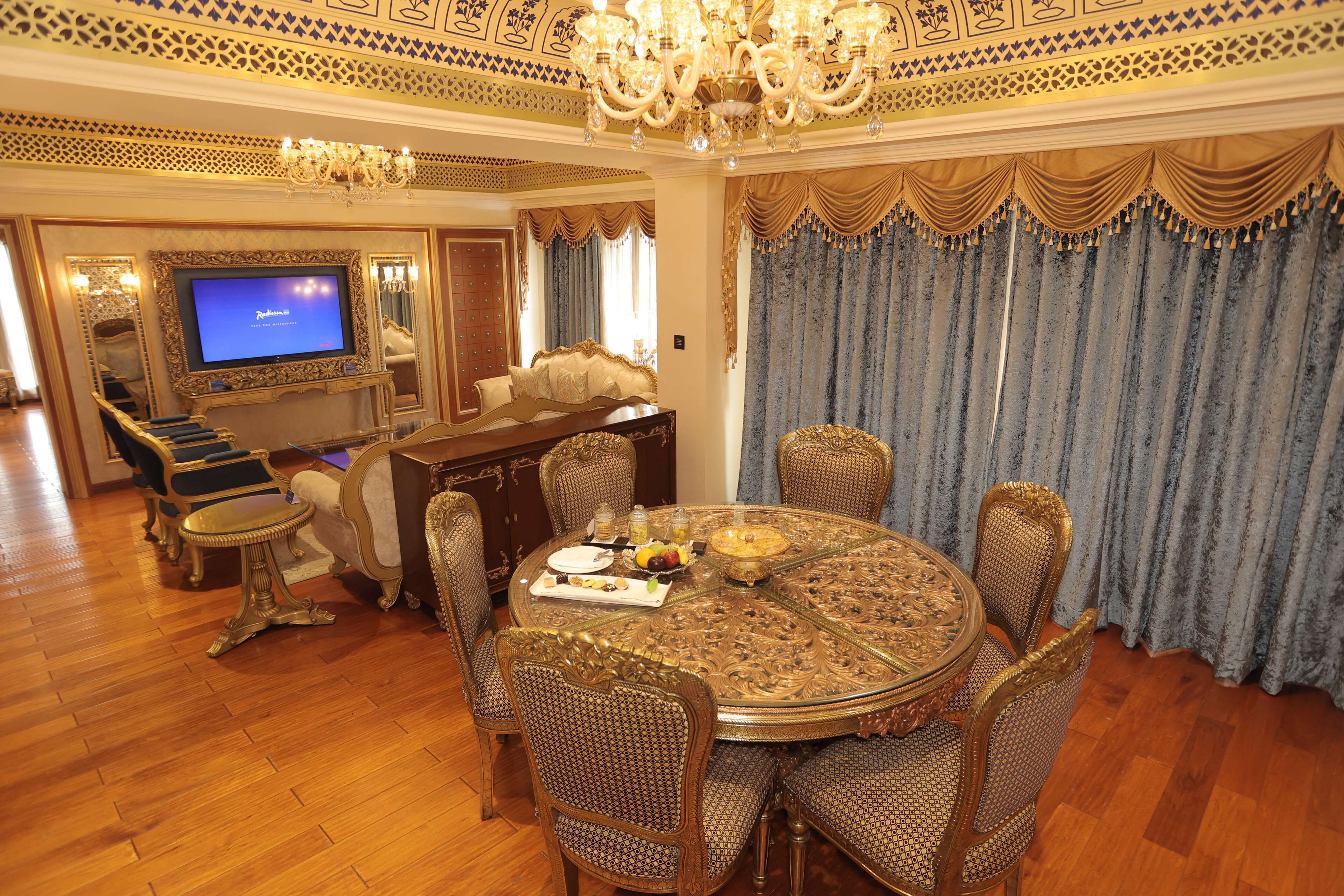 A luxurious dining room with a round table, ornate chairs, and a television in the background.