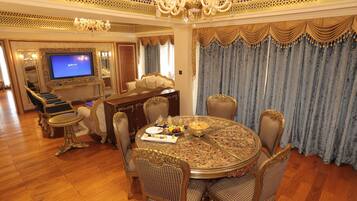 A luxurious dining room with a round table, ornate chairs, and a television in the background.