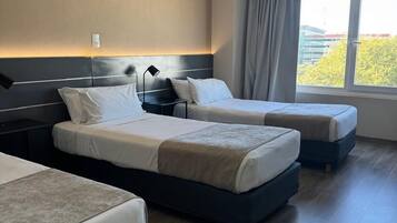 A hotel room with two beds, a large window with curtains, and a view of greenery outside.