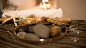 Un décor de spa avec un bol rempli de pierres polies, une étoile de mer, un fagot de branches et une bougie en arrière-plan.
