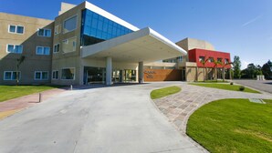 A modern building with a glass facade, a covered entrance, and a red building adjacent to it. - Quórum Cordoba Hotel - Resort Urbano (Córdoba)