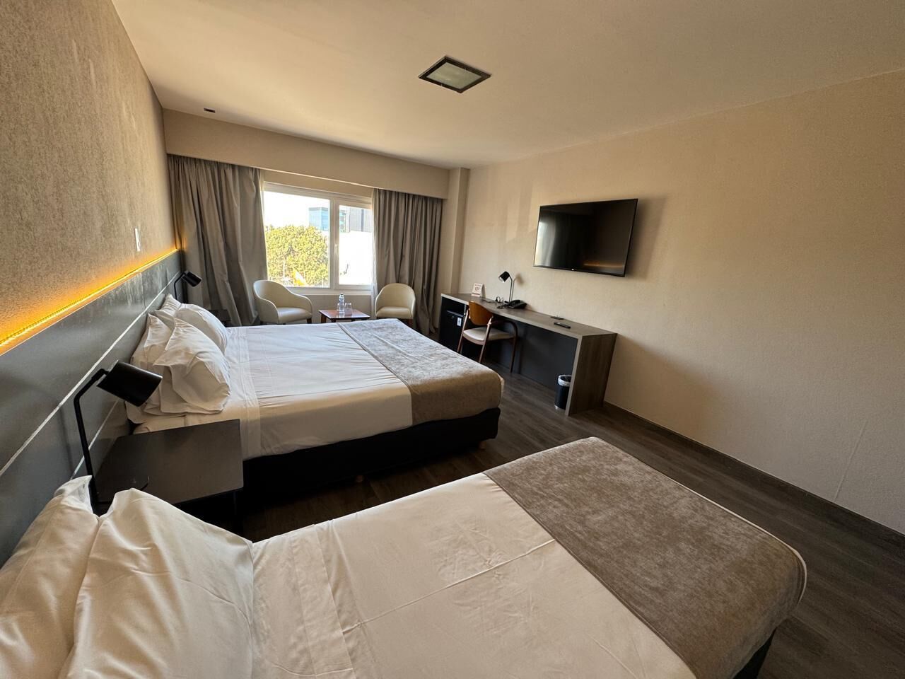 A hotel room with two beds, a desk, a chair, a TV, and a window with curtains.