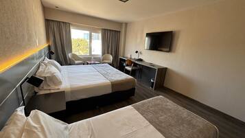 A hotel room with two beds, a desk, a chair, a TV, and a window with curtains.