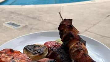 Un plato de carnes y verduras a la parrilla junto a una piscina.