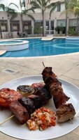 Un plato de carnes y verduras a la parrilla junto a una piscina.