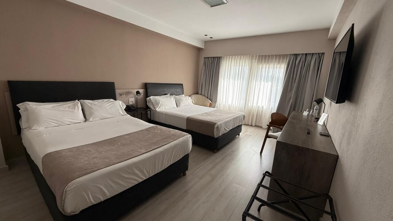 A hotel room with two beds, a desk, and a television.