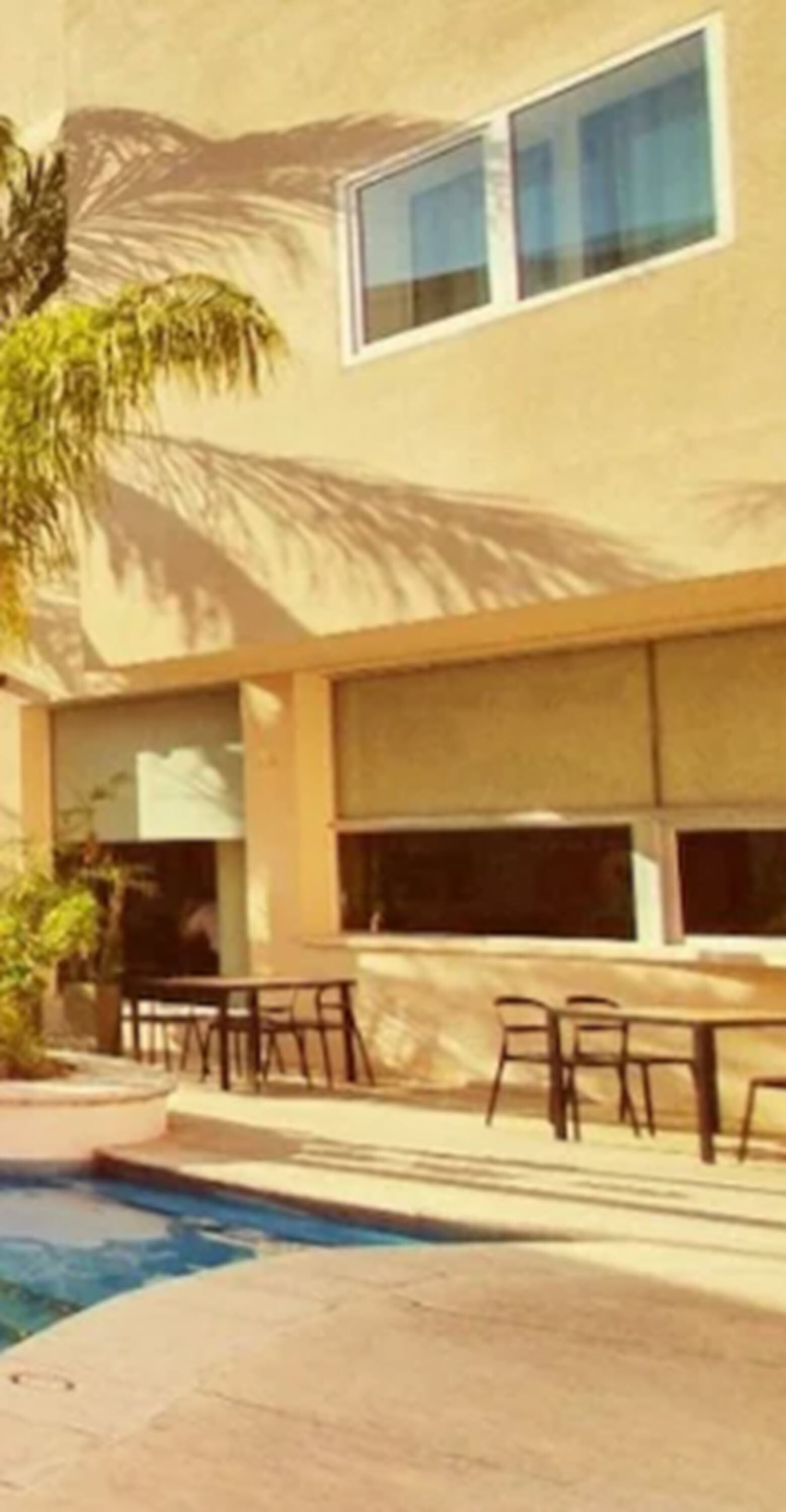 A building with a pool area, outdoor seating, and palm trees.
