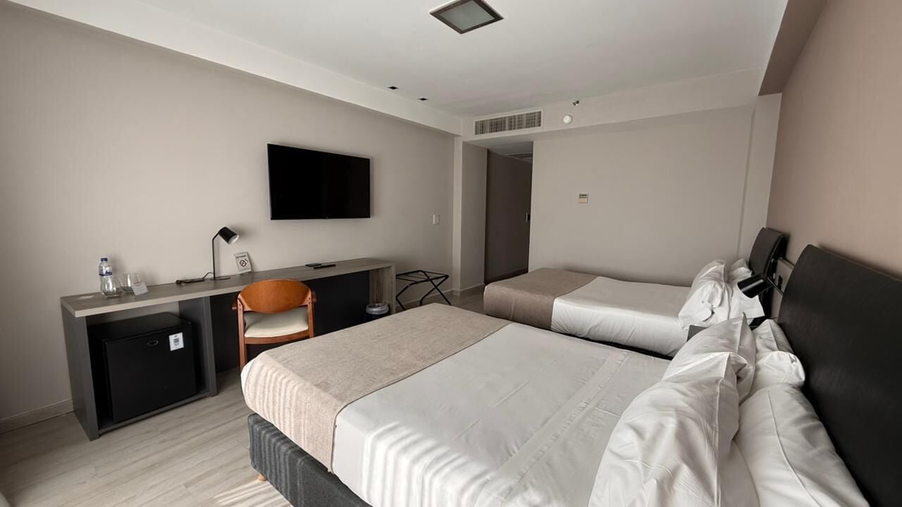 Una habitación de hotel con dos camas, un escritorio, una silla, un televisor y un refrigerador pequeño.