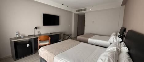 Una habitación de hotel con dos camas, un escritorio, una silla, un televisor y un refrigerador pequeño.