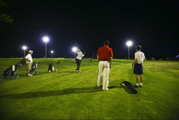 Un campo de golf de noche con personas jugando y bolsas de golf sobre el césped.