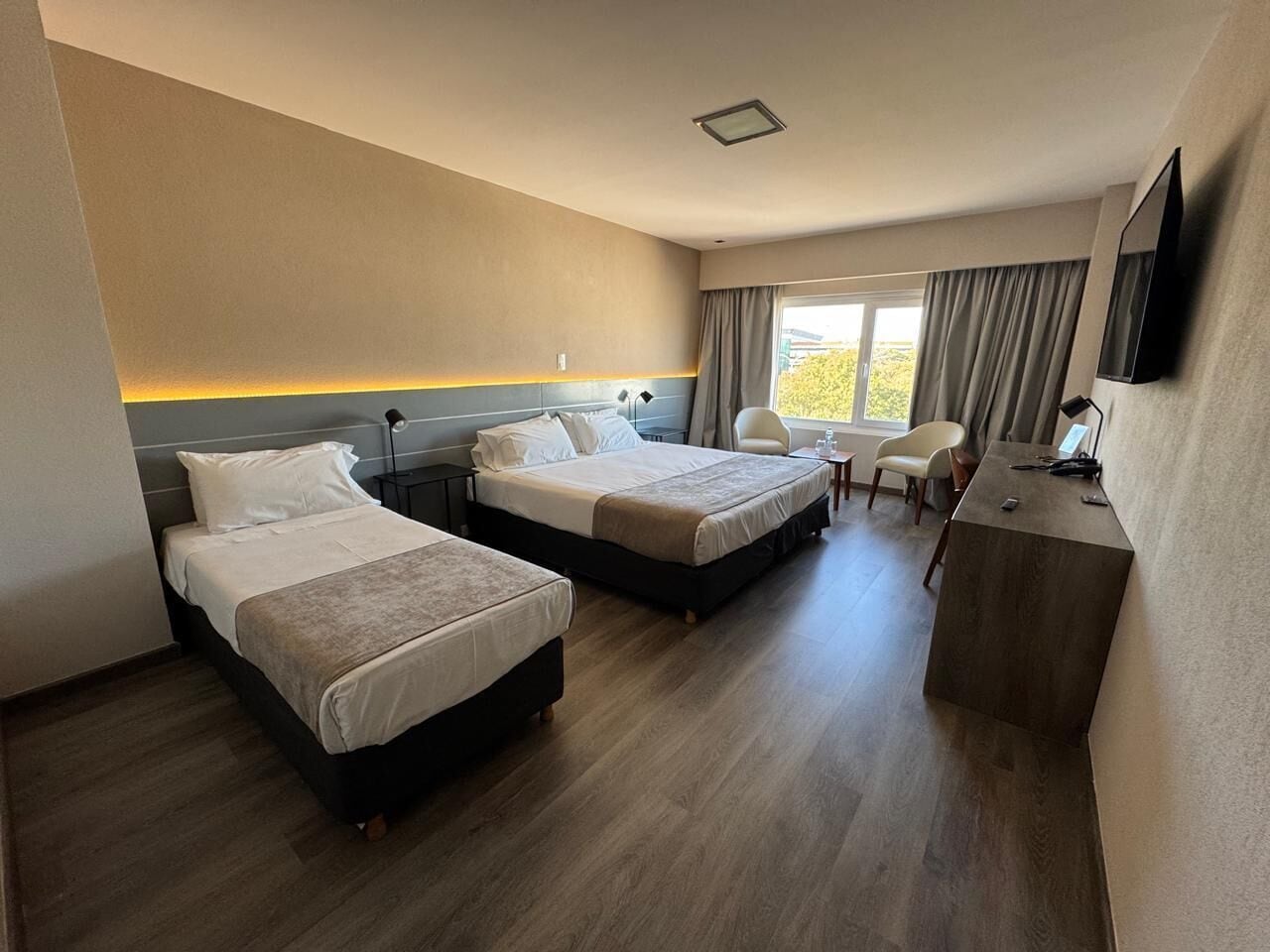 A hotel room with two beds, a desk, a chair, and a large window.