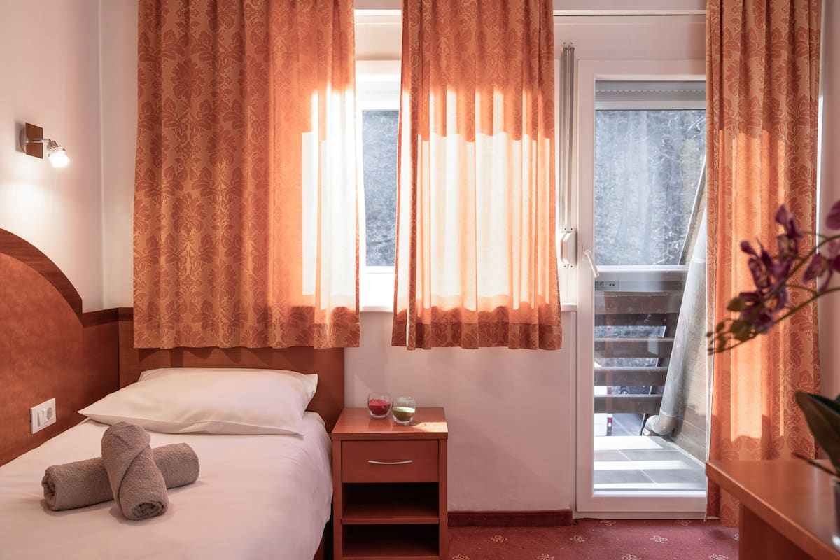 Habitación de hotel con cama, mesita de noche con dos vasos y vistas a un balcón.