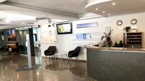 Un área de recepción moderna con un mostrador curvo, asientos, un televisor y arte en la pared.