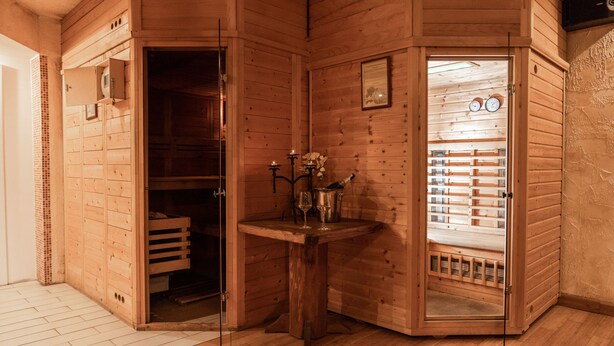 Una sauna de madera con puerta de cristal, una mesita con velas y un reloj en la pared.