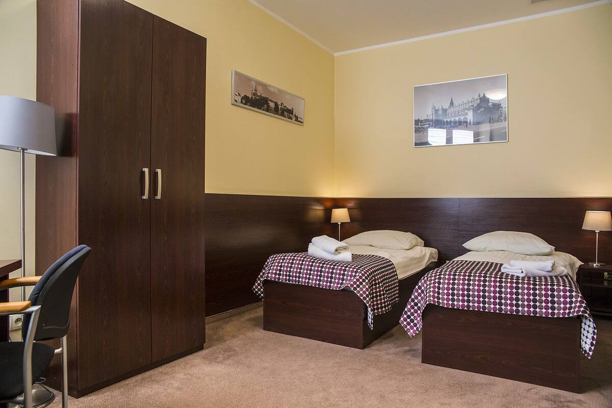 A hotel room with two beds, a wardrobe, and two wall-mounted lamps.