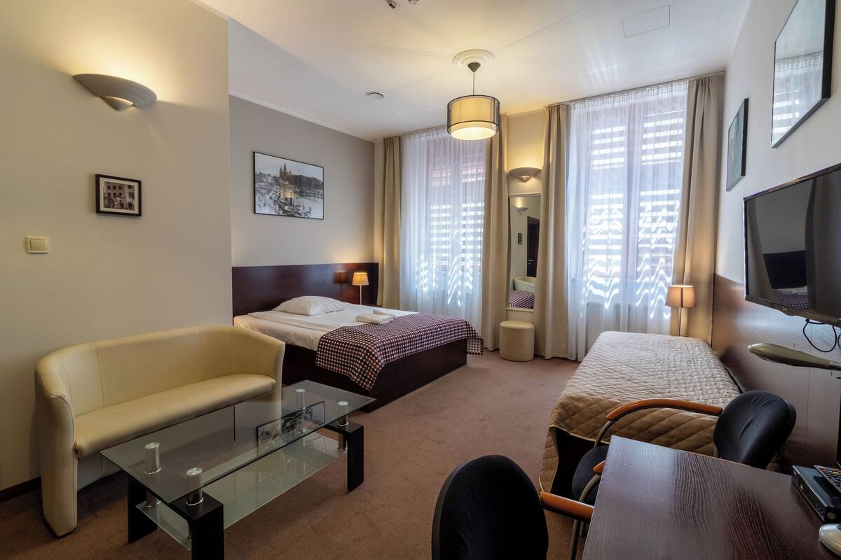 A hotel room with a bed, a sofa, a glass-top table, a TV, and a mirror.