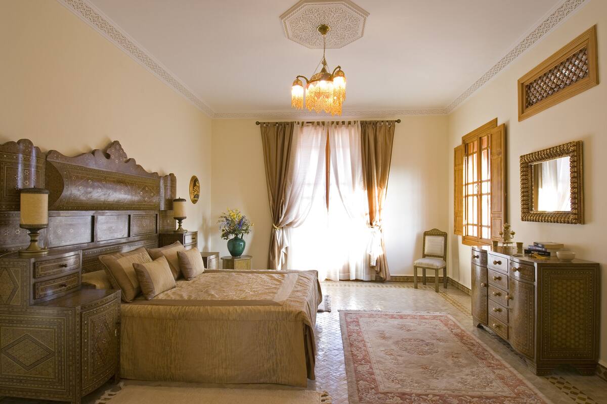 A traditional bedroom with a large bed, ornate headboard, a chandelier, and a classic dresser.