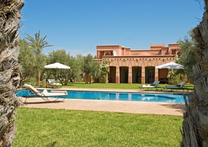 A pool area with lounge chairs and umbrellas, surrounded by a well-maintained lawn and trees. - Dar Kantzaro (Marrakech)