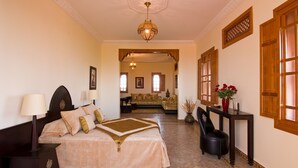 A bedroom with a large bed, a nightstand, a chair, a table, and a hanging light fixture. - Dar Kantzaro (Marrakech)