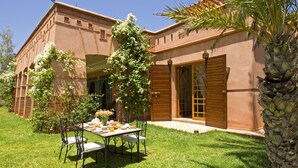 A building with a patio area featuring a table and chairs, surrounded by greenery and a palm tree. - Dar Kantzaro (Marrakech)