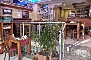 A cozy restaurant with a glass partition, wooden furniture, and various plants.