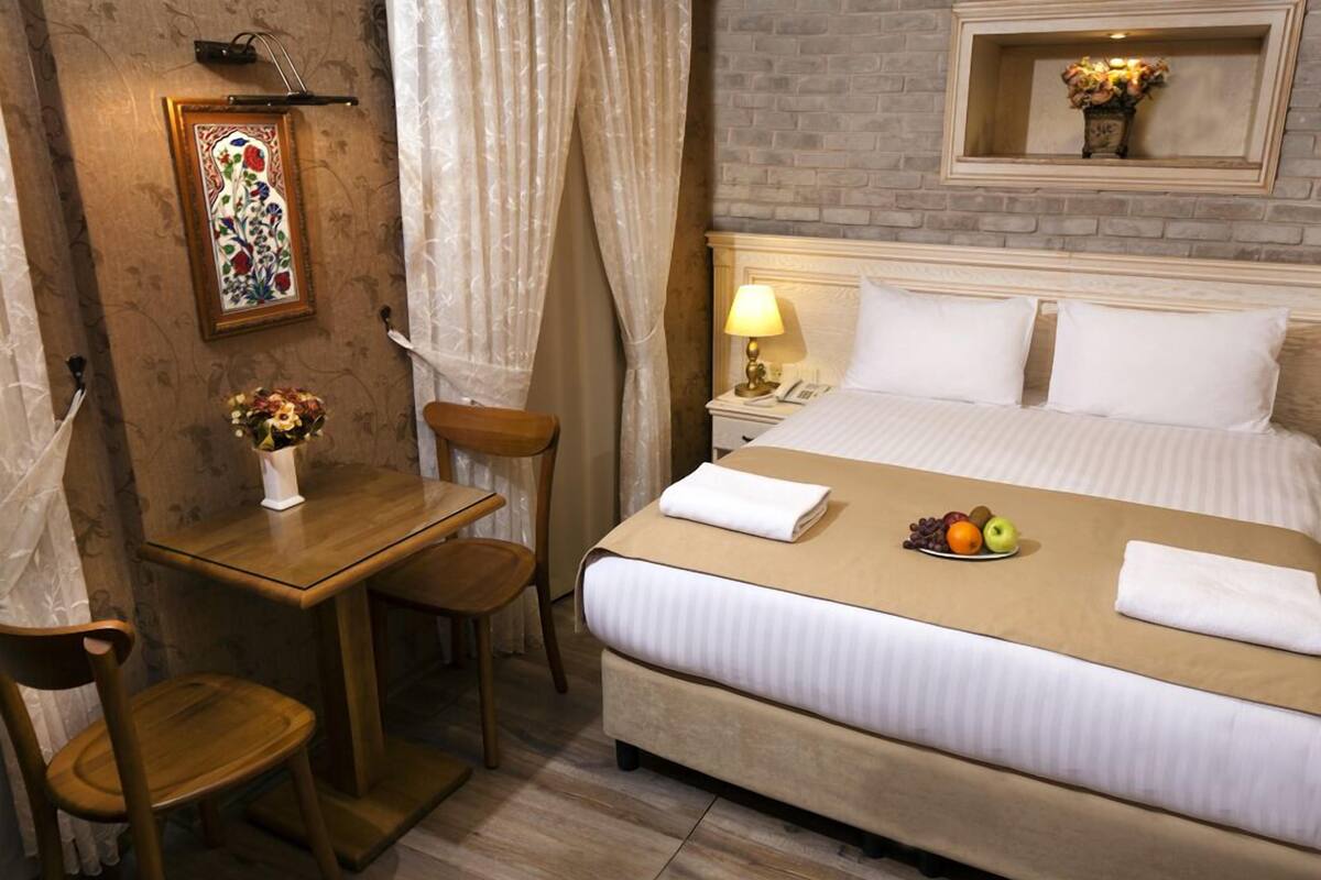 A hotel room with a bed, bedside table, chair, and a small table with a vase of flowers.