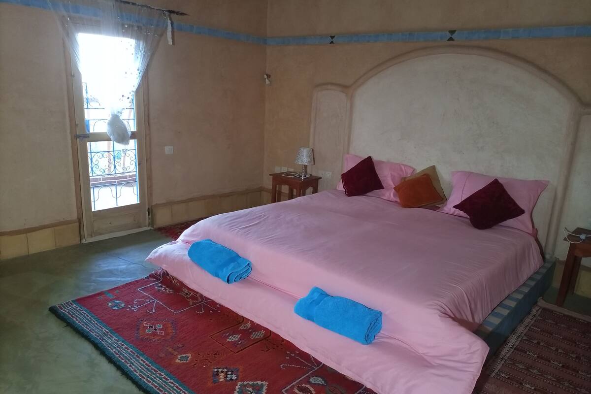 A bedroom with a large bed, a nightstand, a lamp, and a view of the outside balcony.