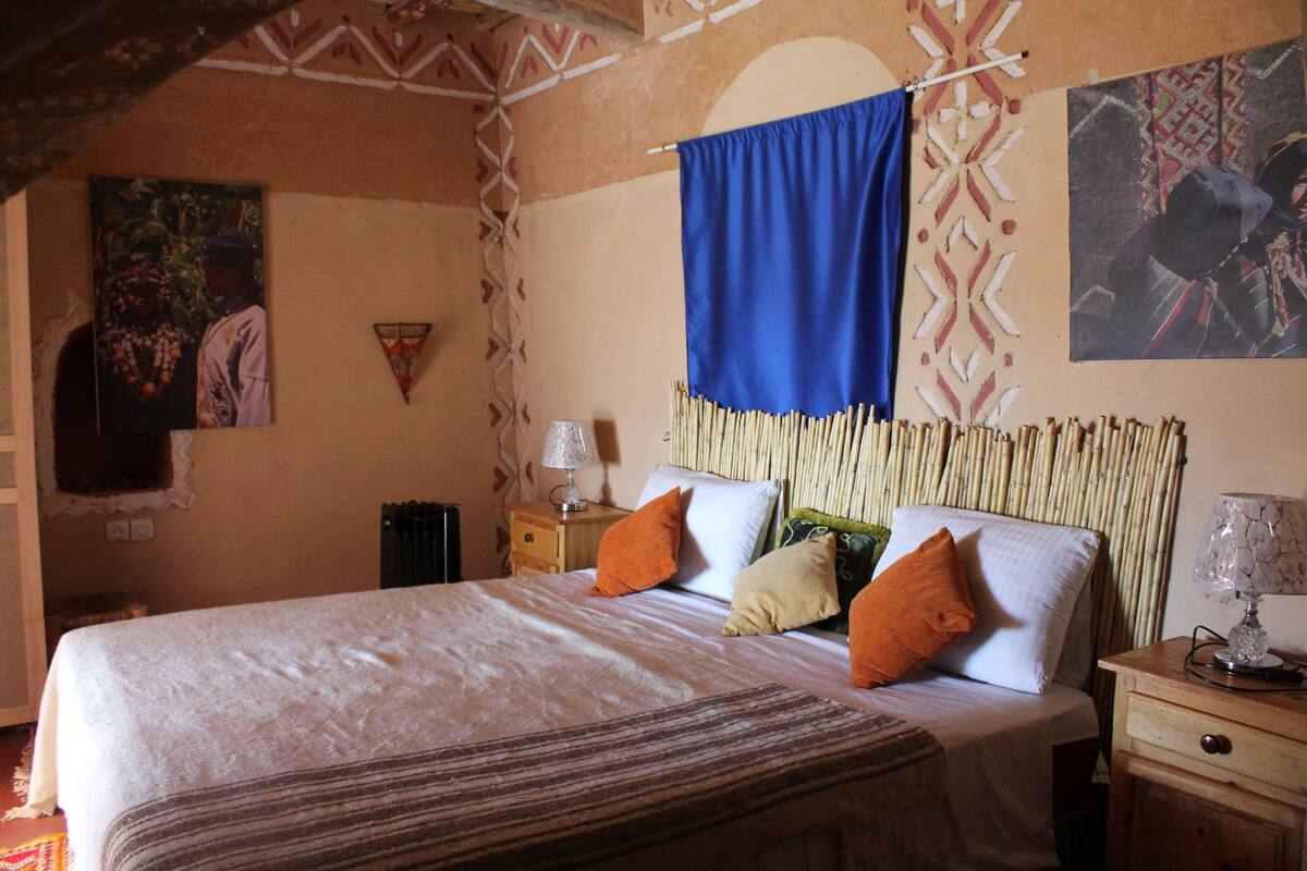 A bedroom with a bed, pillows, a nightstand, and a lamp.