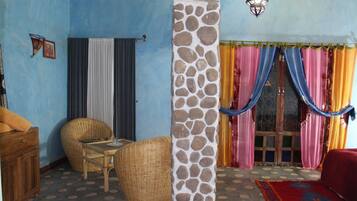Una habitación con pared azul, un pilar de piedra, una silla de mimbre, una mesa de madera y un sofá rojo.