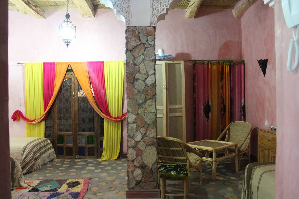 A cozy room with a stone pillar, a bed with striped bedding, and a table with chairs.