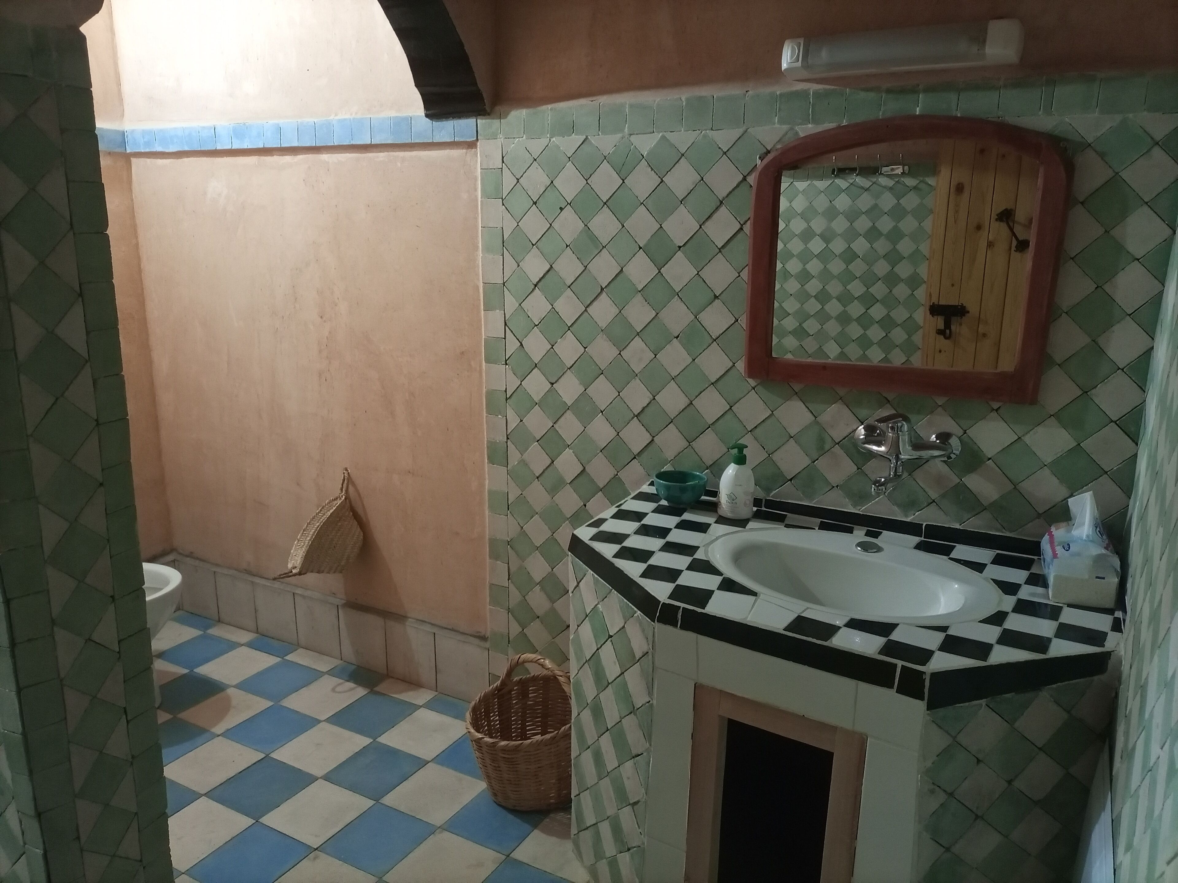 Un bagno con pavimento a scacchi, un lavandino con specchio sopra e un water sullo sfondo.