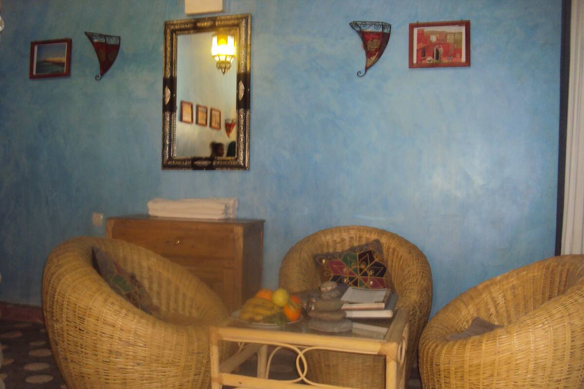 A room with two wicker chairs, a small table with books and fruit, a mirror, and wall decorations.