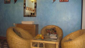 A room with two wicker chairs, a small table with books and fruit, a mirror, and wall decorations.