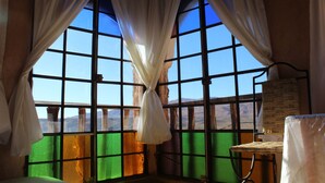 A room with large windows, curtains, a wicker chair, and a small table.