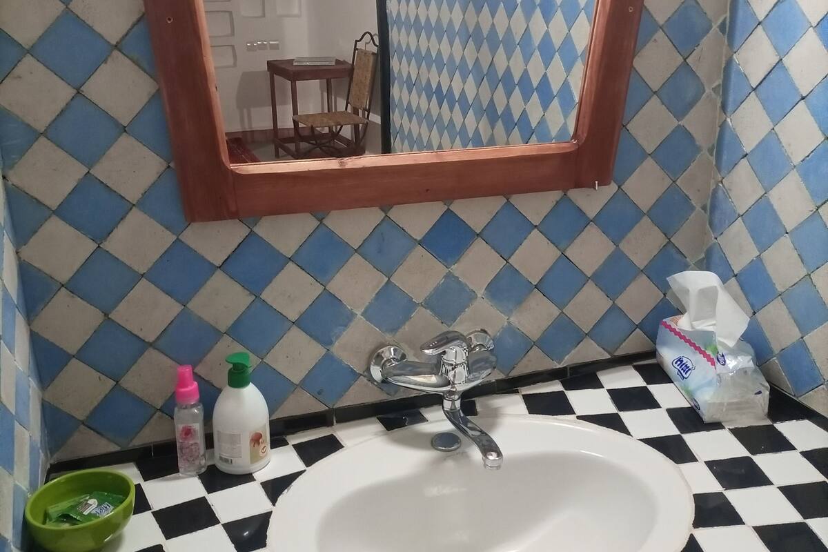 A bathroom with a checkered floor, a white sink, a mirror, and toiletries.