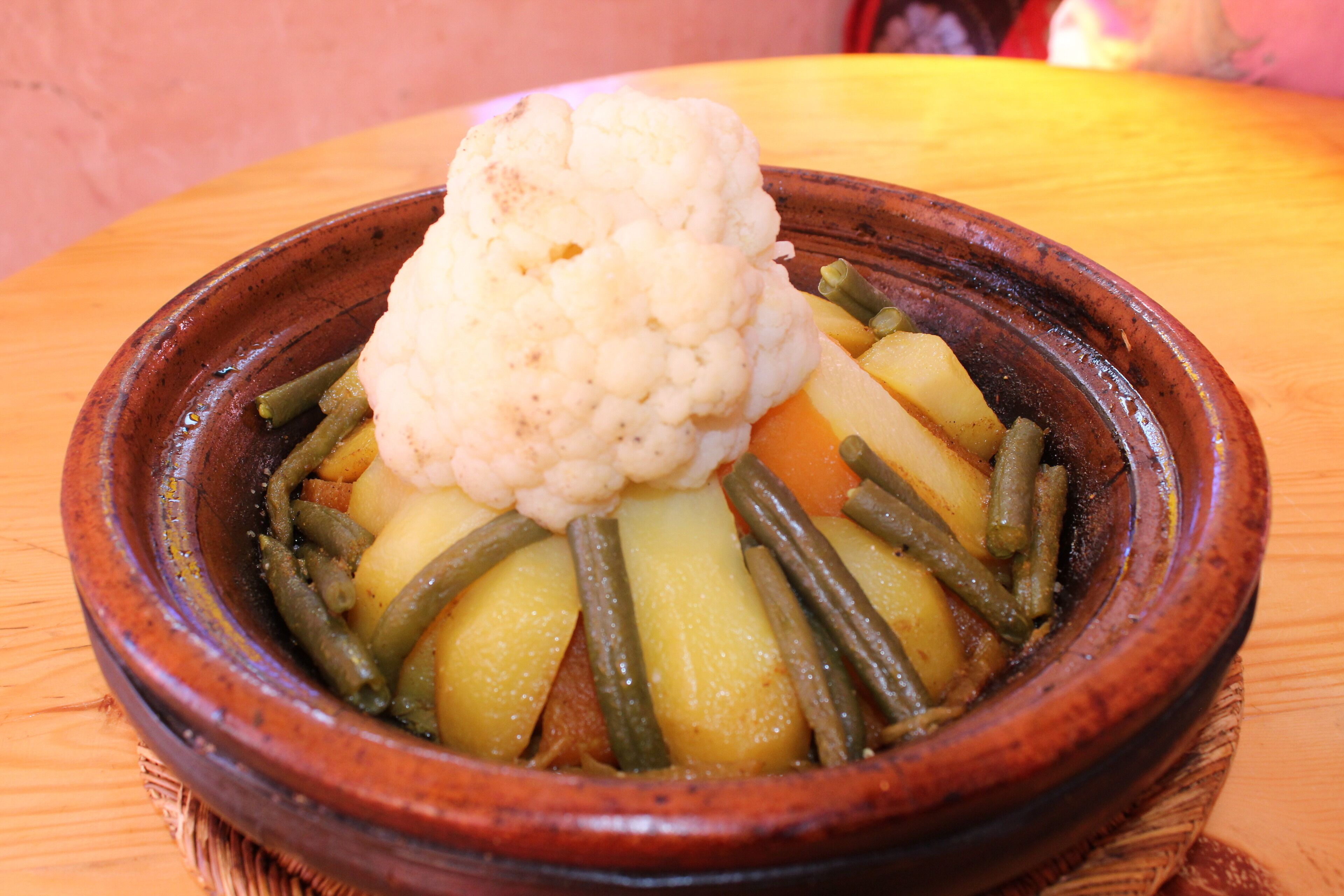 A traditional clay pot filled with a stew of vegetables, including green beans and potatoes, and topped with cauliflower.