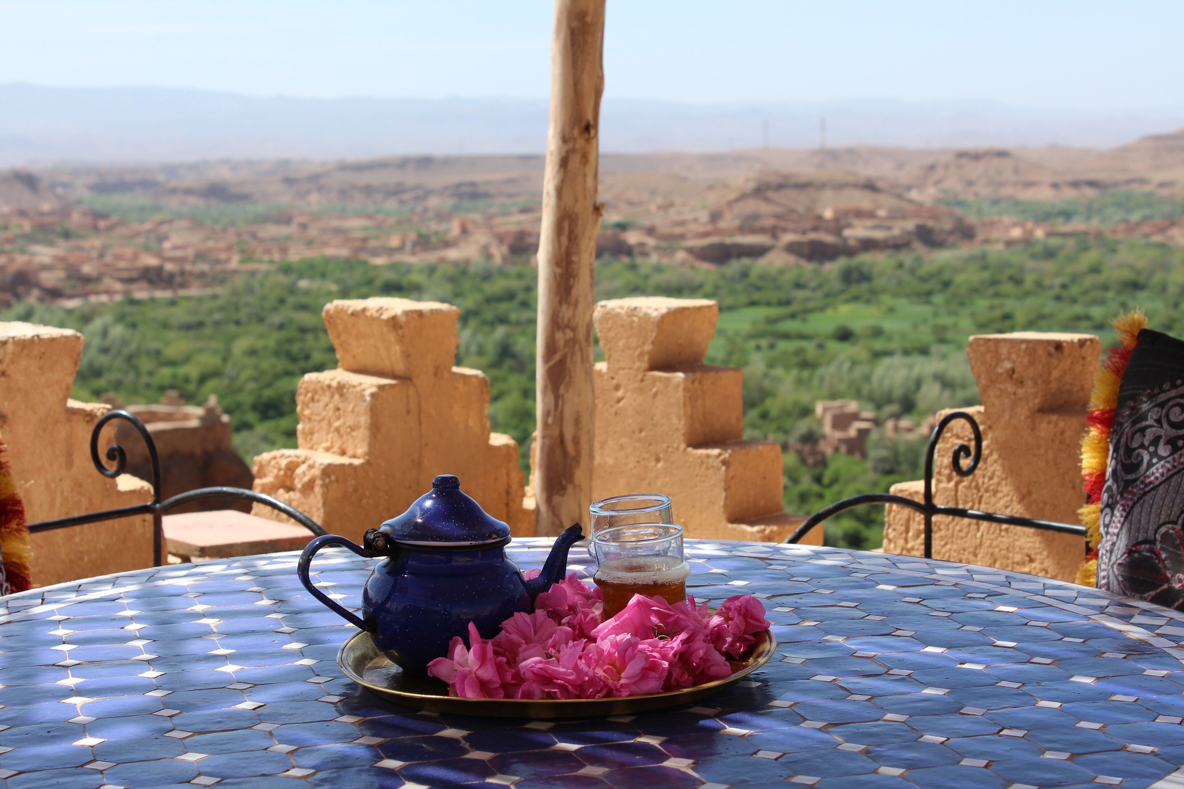 A table with a teapot, a glass of tea, and pink flowers.