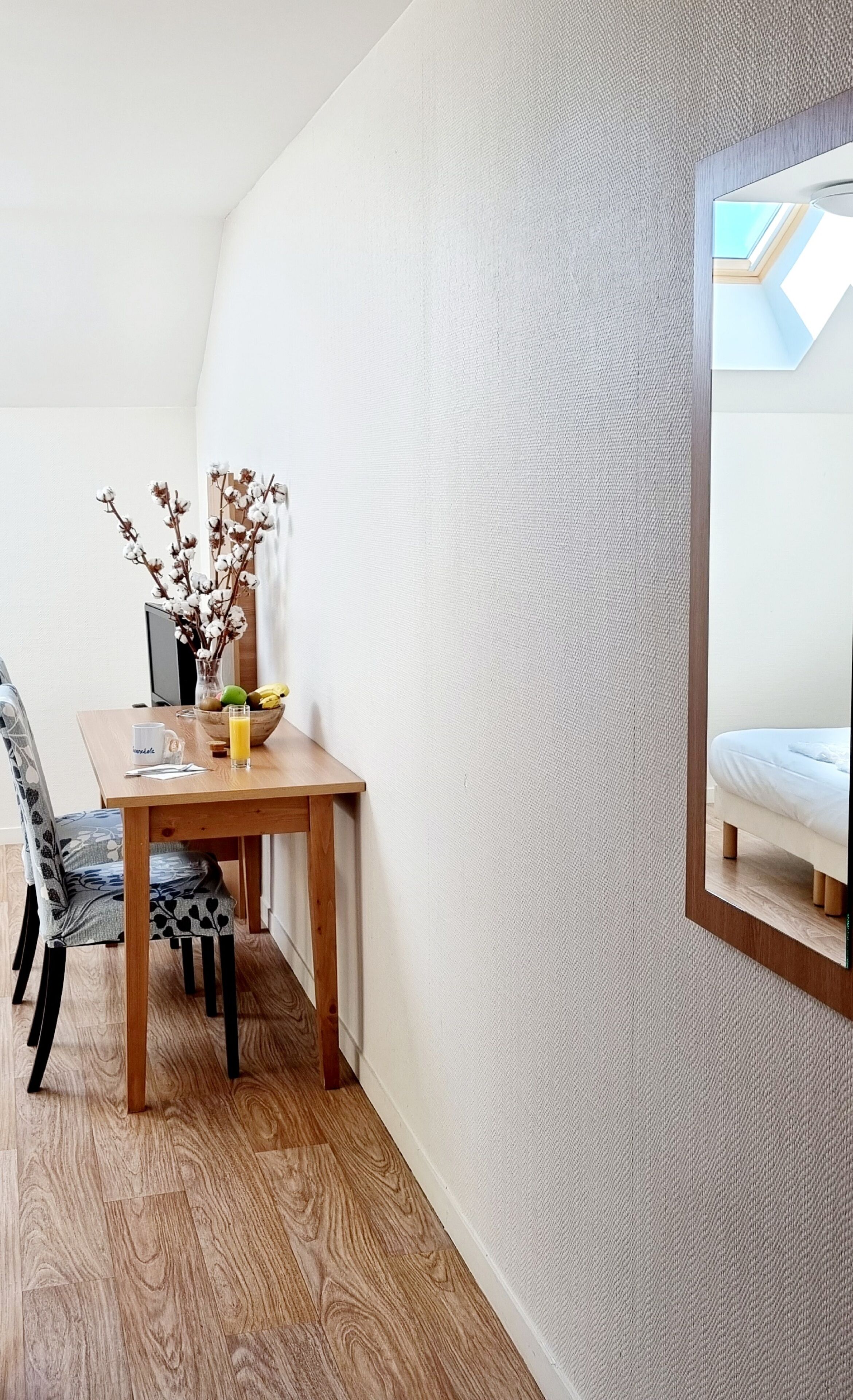 Un coin repas avec une table en bois, des chaises, un vase contenant des fleurs séchées et un saladier rempli de fruits.