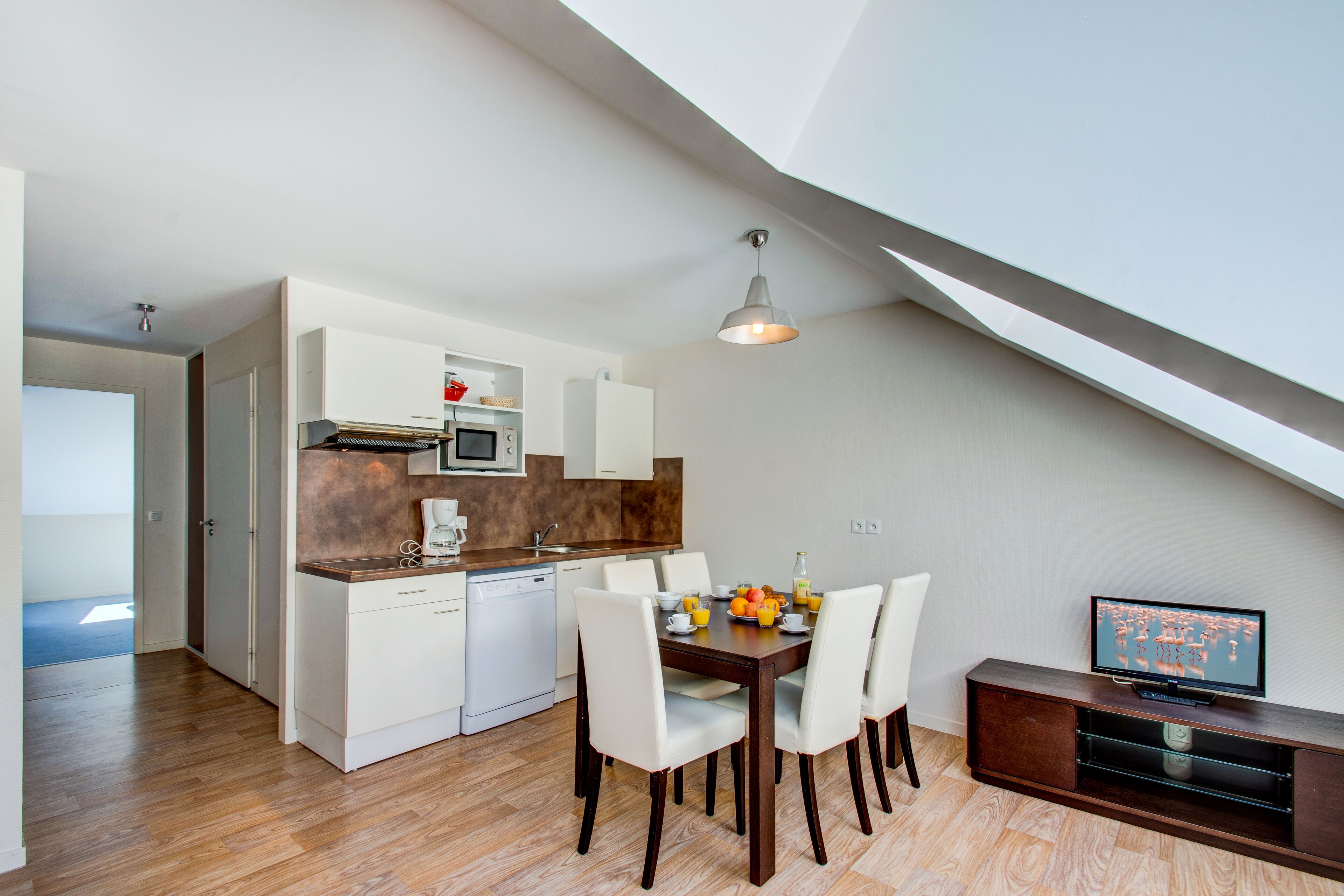 A modern kitchen with white cabinets, a wooden countertop, and a dining area with white chairs.