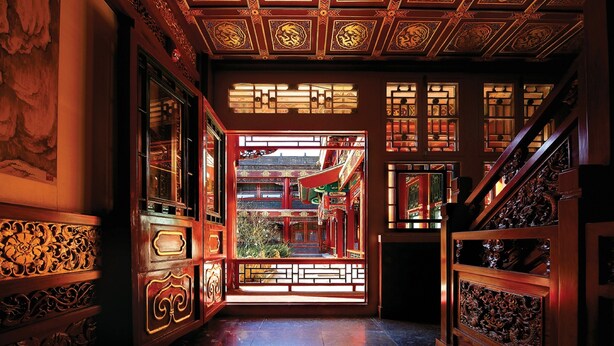 Un corredor ornamentado con elementos arquitectónicos chinos tradicionales, incluyendo detalles tallados intrincados y paneles decorativos.