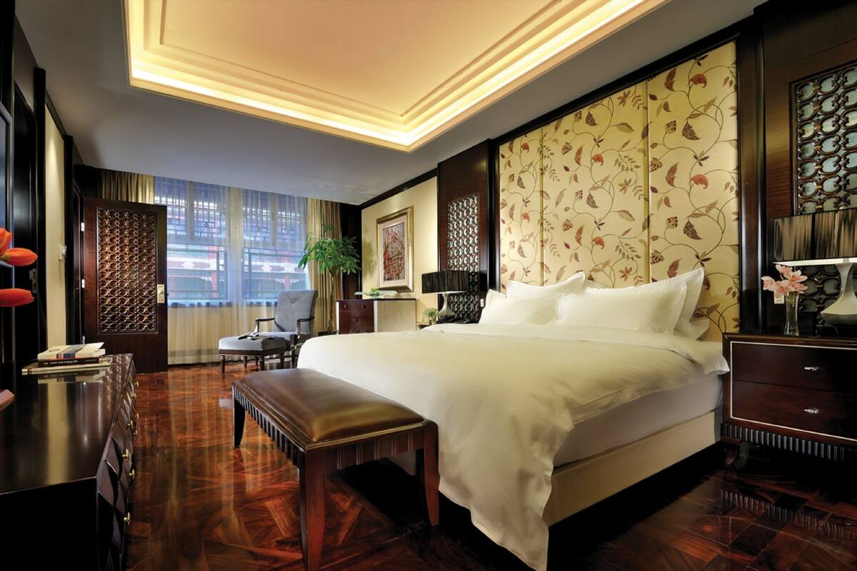 Une chambre d’hôtel avec un grand lit, un bureau avec une chaise, une petite table avec un vase de fleurs et une fenêtre avec des rideaux.