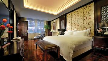 A hotel room with a large bed, a desk with a chair, a small table with a vase of flowers, and a window with curtains.