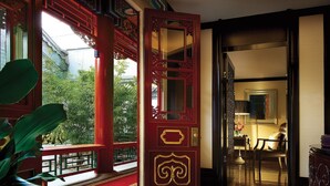 Un interior tradicional con una puerta ornamentada en rojo y dorado, vistas a zonas verdes y una habitación bien iluminada con una mesa y sillas.