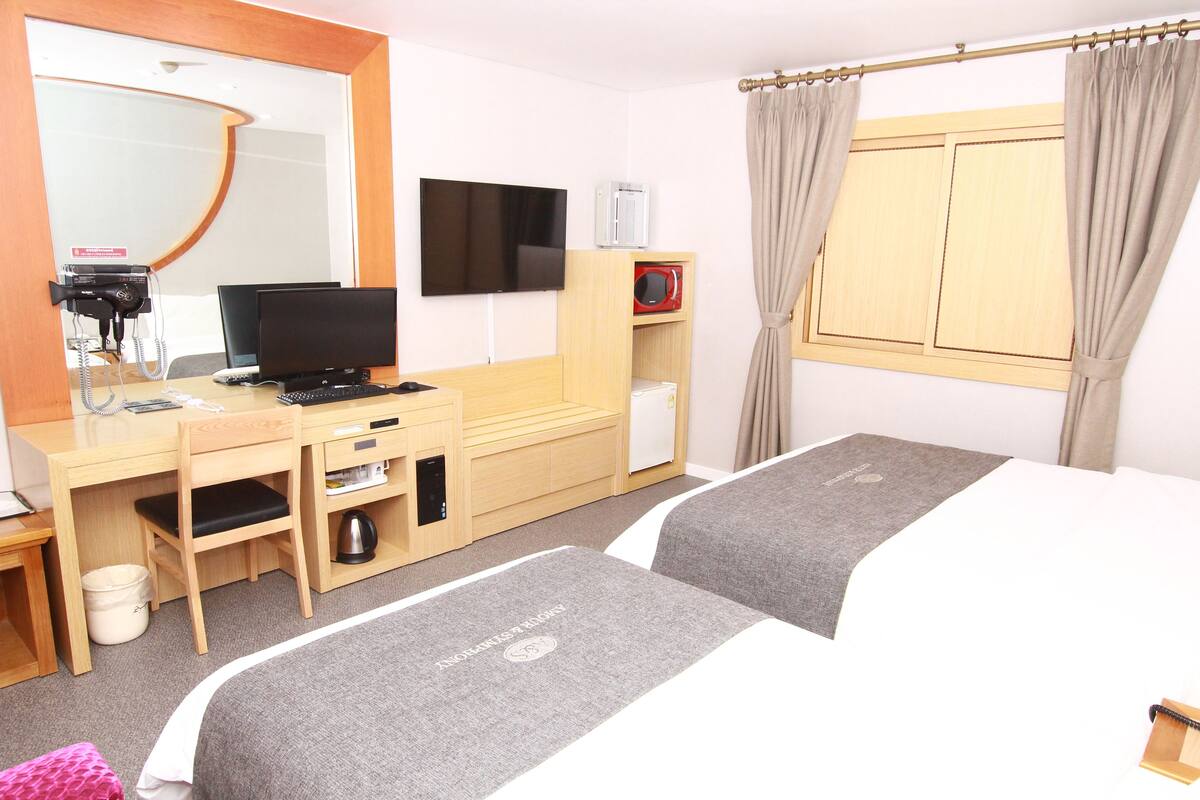 A hotel room with a desk, chair, television, and two beds.