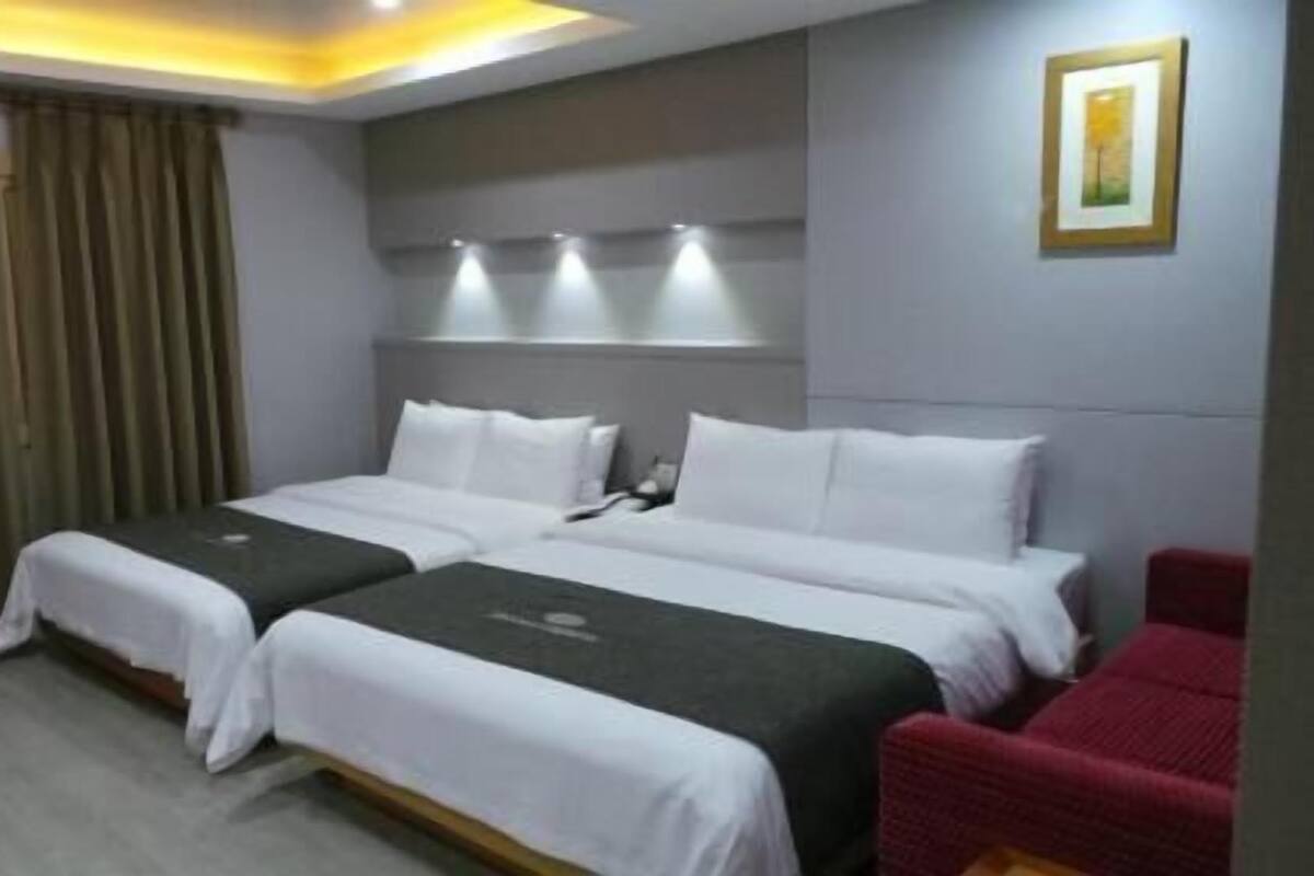 A hotel room with two beds, a red chair, a painting on the wall, and a curtain.