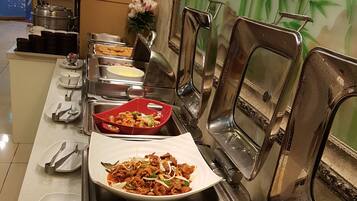 A buffet setup with various dishes, including fried rice and stir-fried vegetables, arranged on stainless steel serving stations.