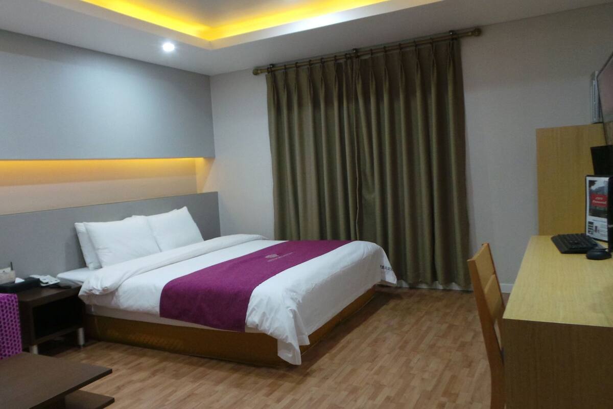 A hotel room with a bed, a desk, a chair, a TV, and a curtain.