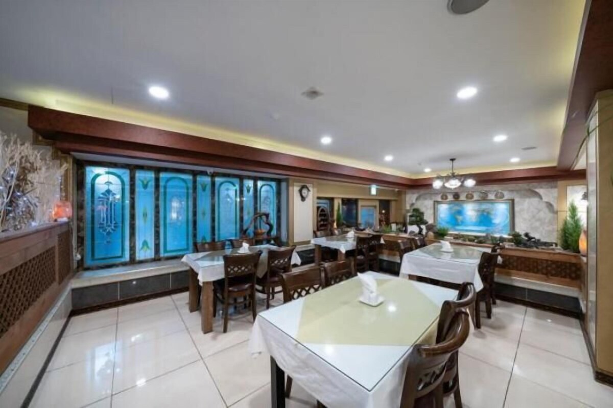 Un restaurante con varias mesas y sillas, piso de baldosas y una pared decorativa con una pantalla grande.